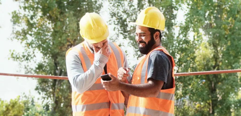 Happy Coworkers Laughing With Smartphone In Construction Site