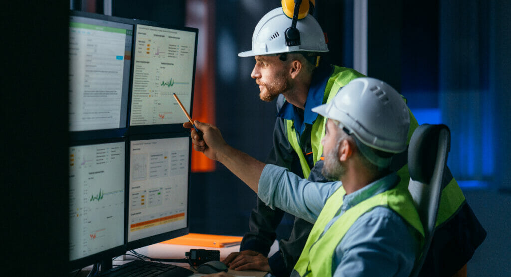 Two construction team members look at data on several computer monitors.