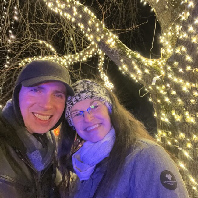 Amanda and her husband standing next to a tree decorated in string lights
